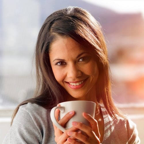 sunrise coffee woman Woman drinking coffee at home with sunrise streaming in through window and creating flare into the lens.